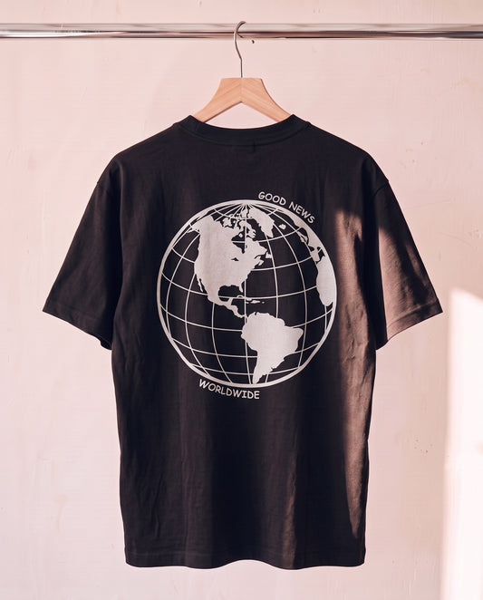 Tell The World Christian tee in black on a wood hanger, back print